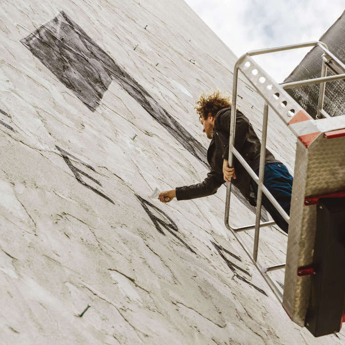 Künstler auf einem Stehlift bringt in der Höhe den Spezialputz an der Hauswand an