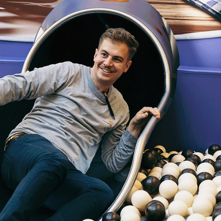 Mann rutsch in ein Bällebad. Dabei wird er fotografiert. Das Foto kann direkt ausgedruckt werden.